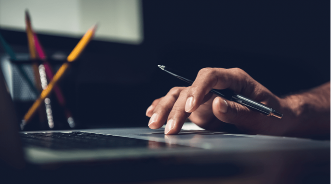 Hand holding a pen while using a laptop track pad