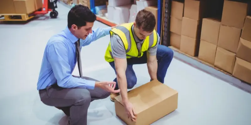 Warehouse manager educating employee on the correct way to lift a heavy box