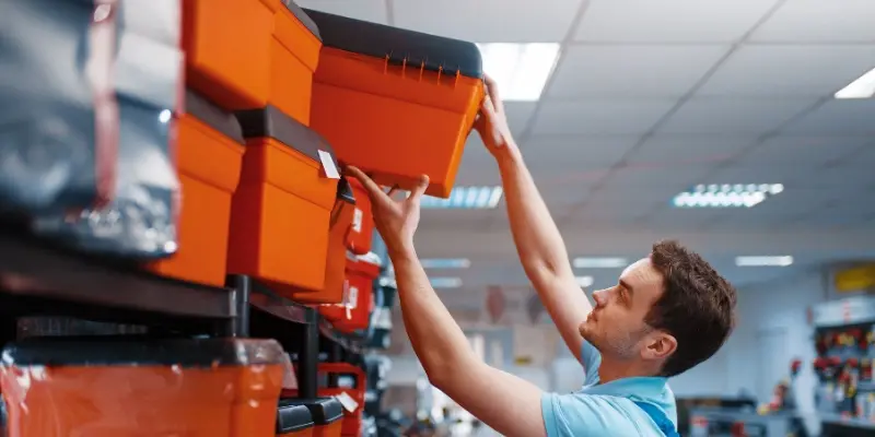 Worker grabbing heavy box with merchandise from top shelf