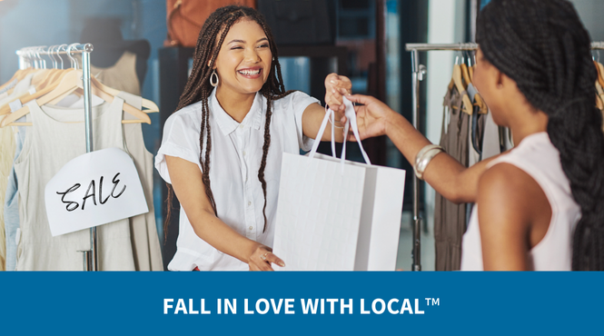 A female retail employee handing a customer her purchase, smiling with a 